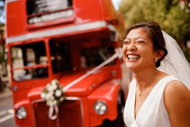 Candid wedding photo of a very happy bride in front of a red London bus by wedding photographer ARJ Photography®