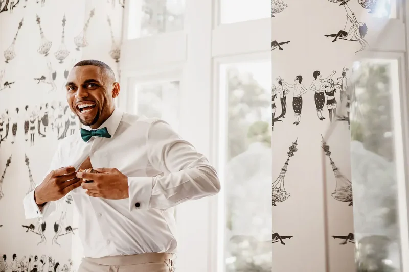 Candid wedding photo of the groom laughing as he puts aftershave on while getting ready for the wedding by wedding photographer ARJ Photography®