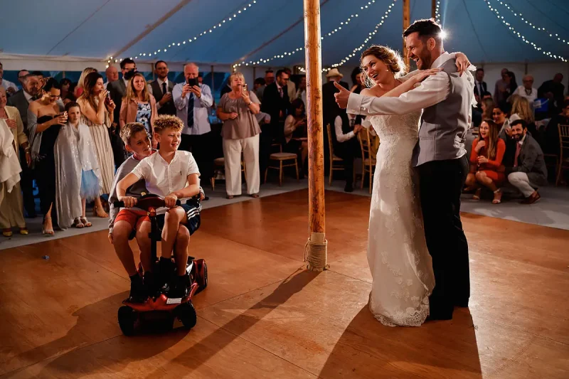 Candid wedding photo of a first dance where the bride and groom's son has come onto the dance floor riding a mobility scooter by wedding photographer ARJ Photography®