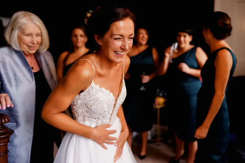 Candid wedding photo of a very happy bride putting her wedding dress on by wedding photographer ARJ Photography®