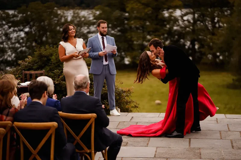 A truly iconic wedding ceremony moment at this outdoor wedding ceremony as bride and groom have their first kiss while friends watch on by wedding photographer ARJ Photography®