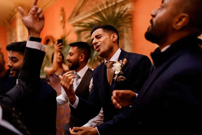 Wedding party candid moment as the groom sings and dances with his bridal party and friends in the Cotswolds UK by wedding photographer ARJ Photography®