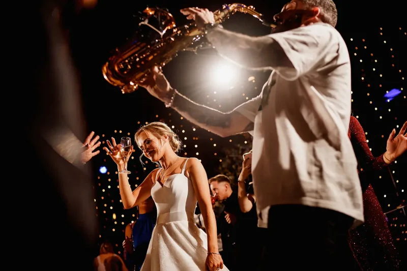 Epic wedding party photo as a bride dances with her friends while a live saxophone player entertains by wedding photographer ARJ Photography®