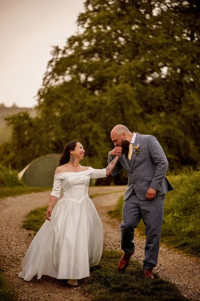 A groom kisses his bride on the hand in the rain during their wedding portraits in the Peak District UK by wedding photographer ARJ Photography®