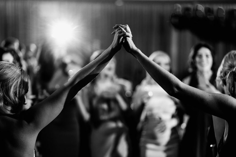A dance floor wedding moment as the bride and a bridesmaid hold hands in the air - powerful black and white wedding photography by ARJ Photography®