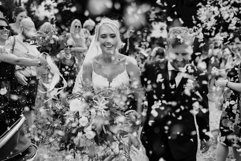 A black and white wedding confetti photo with a very happy bride and groom - powerful black and white wedding photography by ARJ Photography®