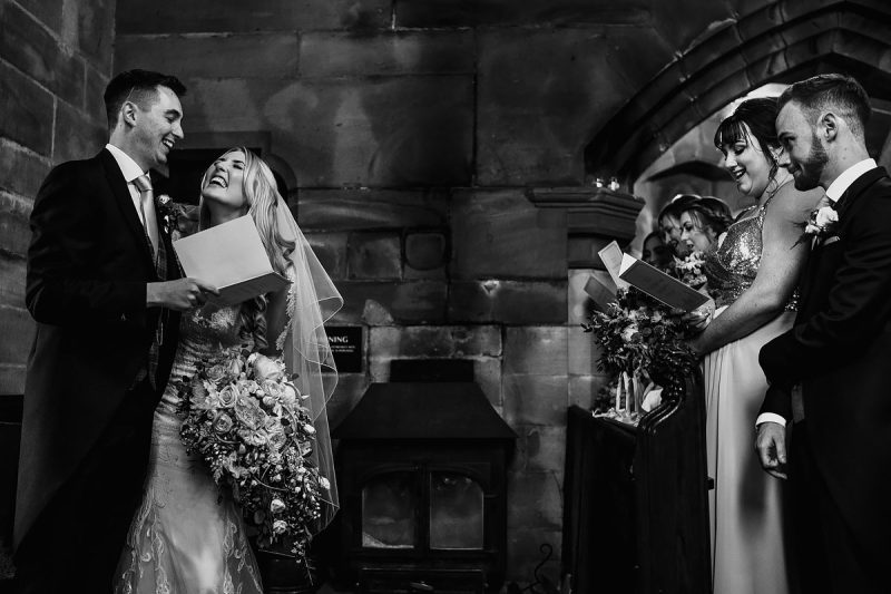 A fun moment between the bride and groom as the guests look on during a church wedding ceremony - powerful black and white wedding photography by ARJ Photography®