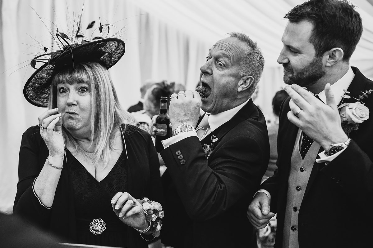 A funny moment captured as the groom and his parents eat some canapes at a marquee wedding - powerful black and white wedding photography by ARJ Photography®