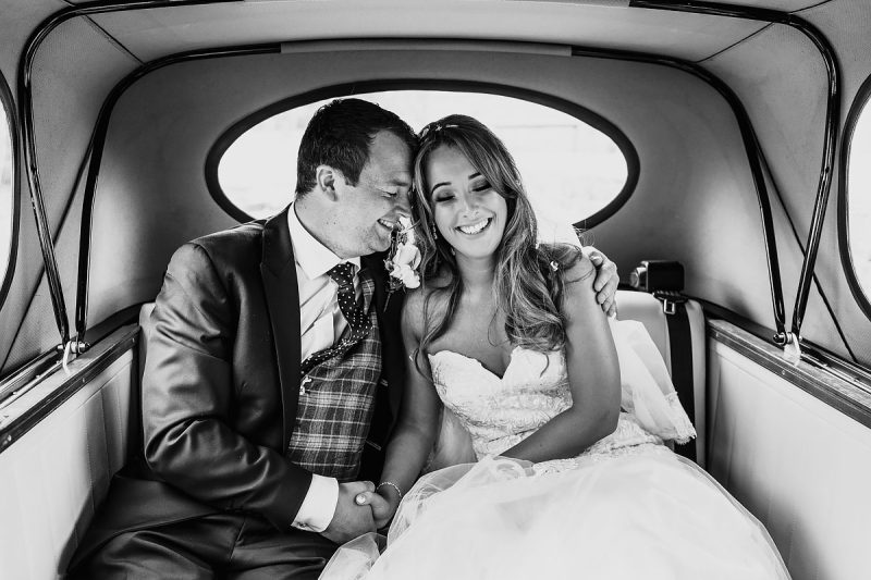 A bride and groom having a happy moment in the back of the wedding car - powerful black and white wedding photography by ARJ Photography®