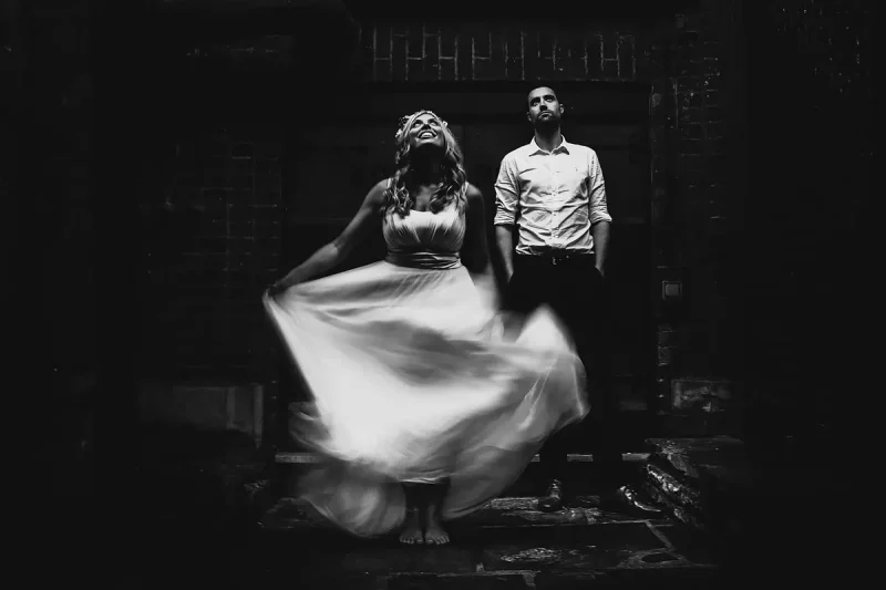 Quirky and unique black and white portrait of a bride and groom with the bride swishing her wedding dress - artistic wedding photography by ARJ Photography®