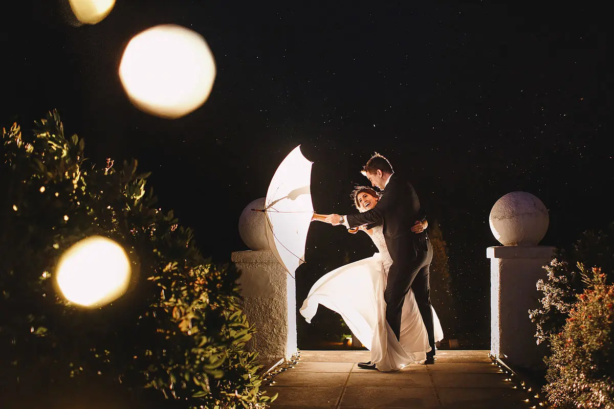 Windy and dramatic wedding photo of a bride and groom having fun and holding an umbrella in the Scottish Highlands - artistic wedding photography by ARJ Photography®