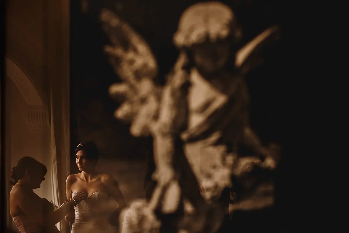 A bride reflected in some artwork of an angel while she gets ready for her wedding ceremony - artistic wedding photography by ARJ Photography®