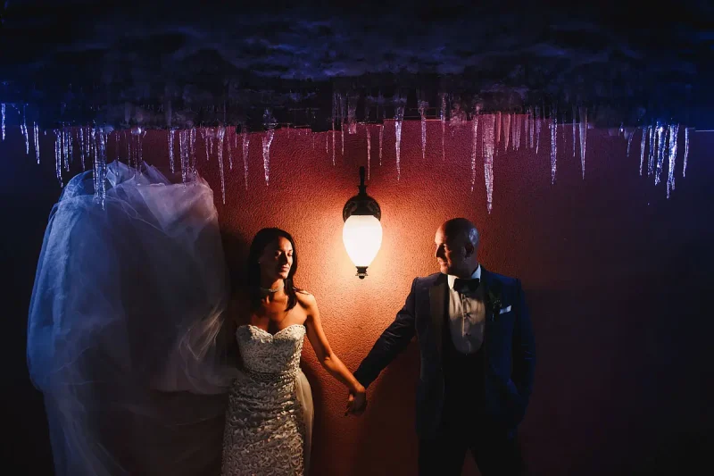 A creative wedding portrait of a bride and groom at a winter wedding with icicles above and the bride's wedding dress being swished - artistic wedding photography by ARJ Photography®