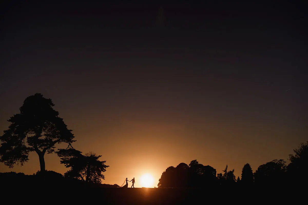 A tiny sunset silhouette of a bride and groom on their wedding day - artistic wedding photography by ARJ Photography®