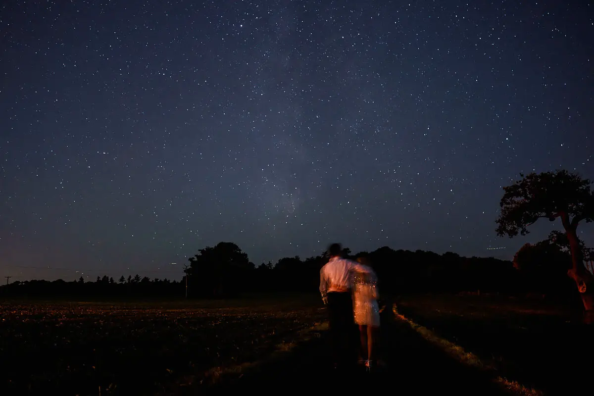A bride and groom walk away at the end of the night under a starry sky creating a blurred effect - artistic wedding photography by ARJ Photography®