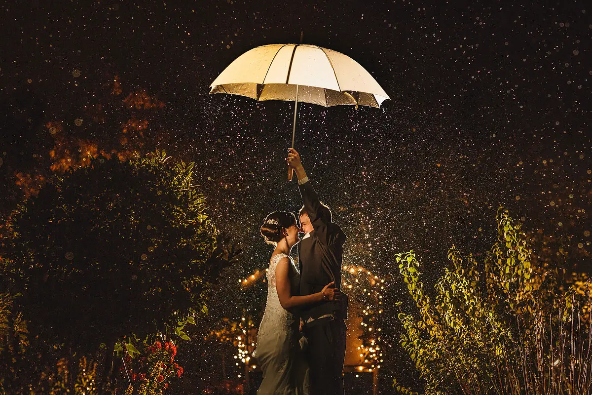 Rainy wedding day portrait of a bride and groom under an umbrella having fun - artistic wedding photography by ARJ Photography®