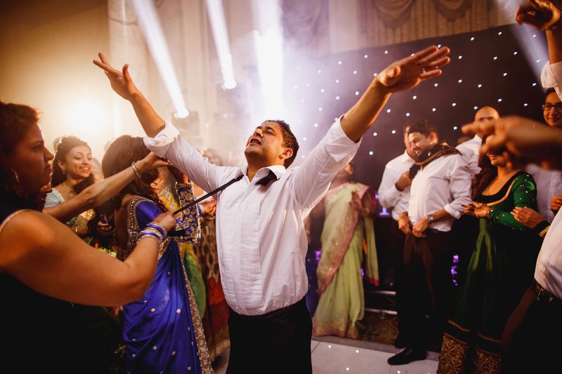 A groom enjoying life on the dance floor at his wedding as a guest pulls on his bow tie - epic wedding party photo by ARJ Photography®