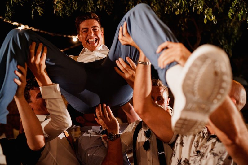 A groom is lifted up by his friends at a destination wedding in Greece - epic wedding party photo by ARJ Photography®