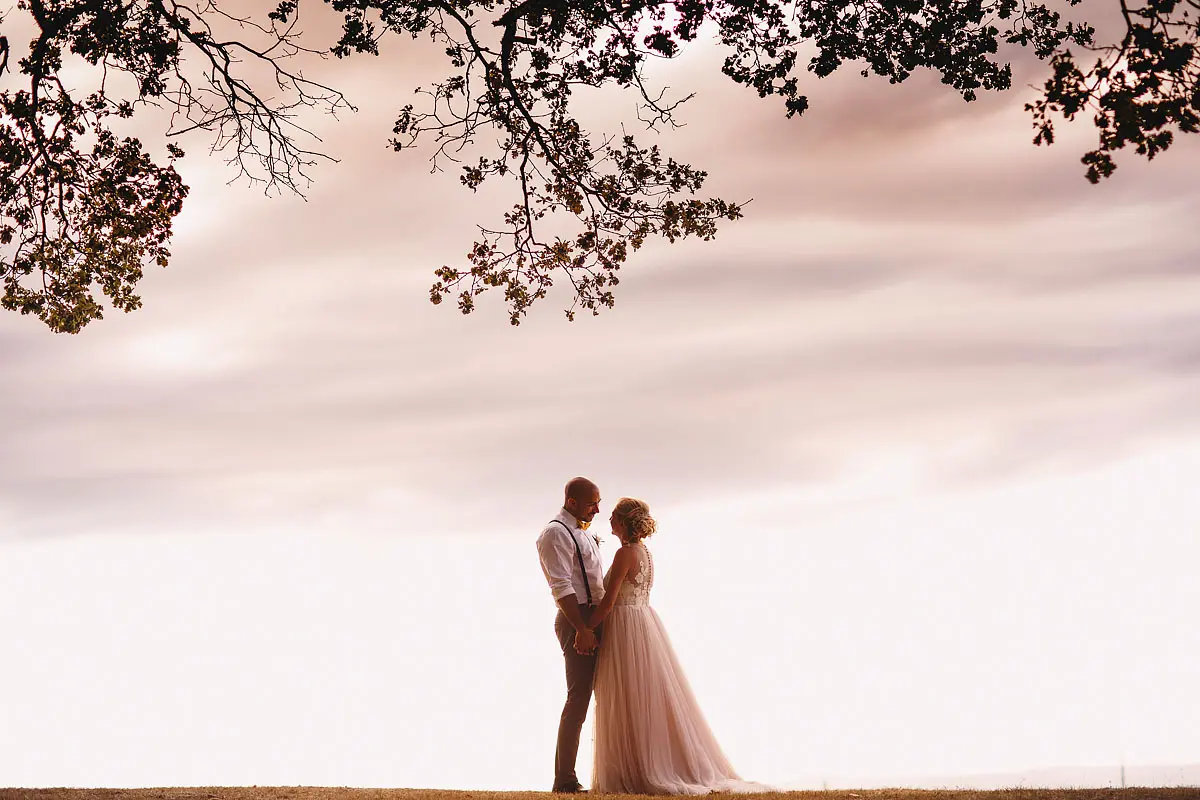 A bride and groom share a romantic moment on top of a hill under a tree at a destination wedding in Tuscany Italy by destination wedding photographer ARJ Photography®