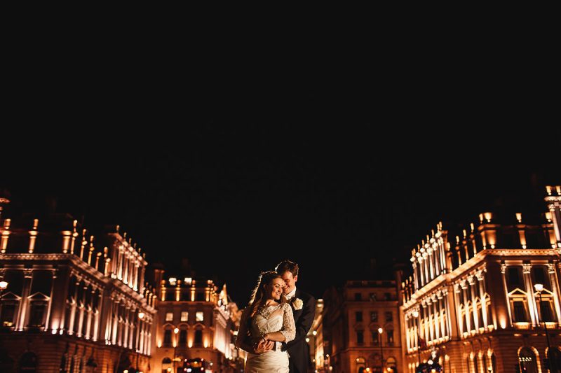 A bride and groom framed artistically by buildings at night in London after their wedding - incredible wedding portraits by ARJ Photography®
