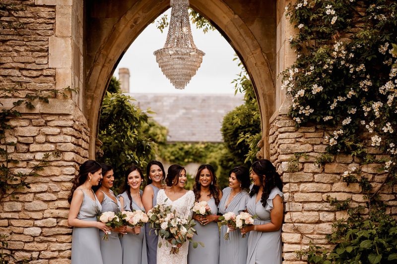 Bride and Bridesmaids laughing at Euridge Manor in the Cotswolds with an outdoor chandelier overhead - incredible wedding portraits by ARJ Photography®