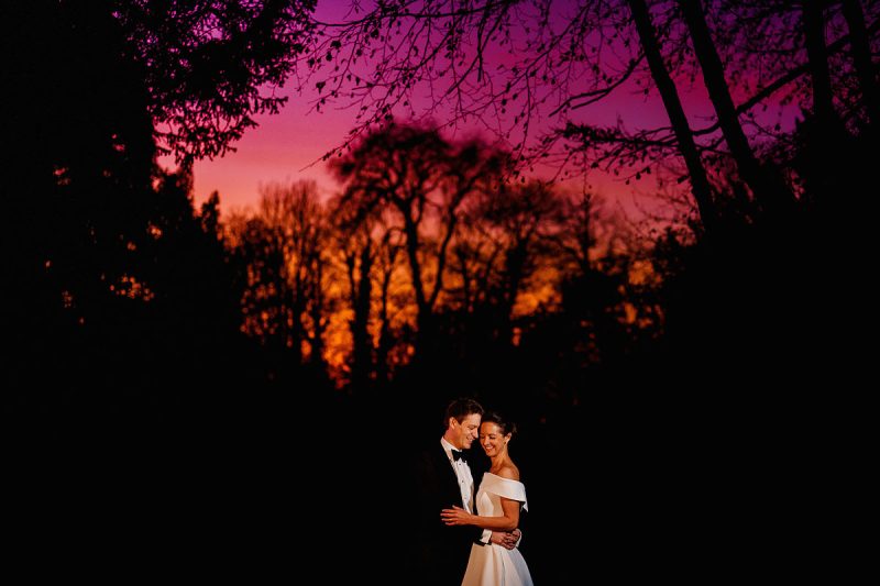 A bride and groom at night with a pink and orange sky after sunset - incredible wedding portraits by ARJ Photography®