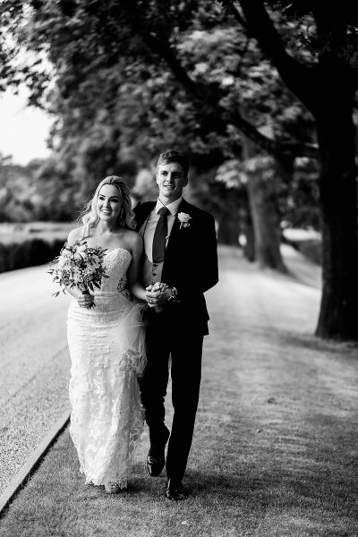 Natural black and white portrait of a groom and bride walking through the grounds of their wedding venue and smiling - incredible wedding portraits by ARJ Photography®