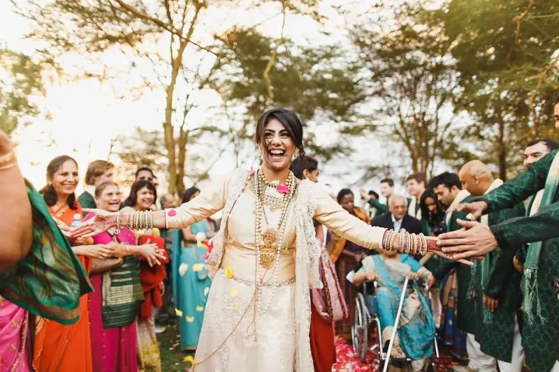 A happy vidai moment as this bride smiles and high fives her way out of the Hindu destination wedding ceremony in Naivasha Kenya - Unique Indian wedding photos by ARJ Photography®