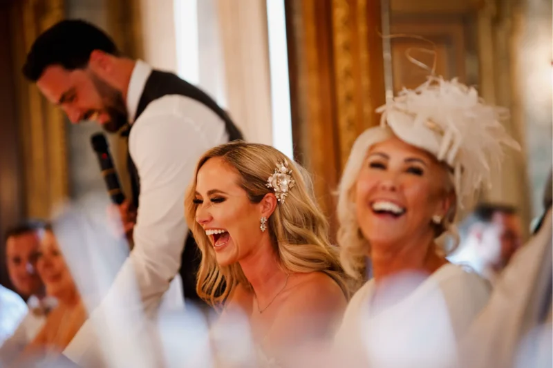 Bride and mother of the bride laughing during the groom's speech at a Hawkstone Hall wedding.